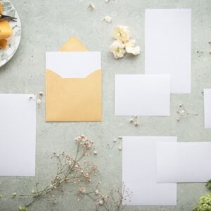 A flat lay of blank stationery and envelope amidst delicate flowers and ribbon, perfect for wedding or event planning.
