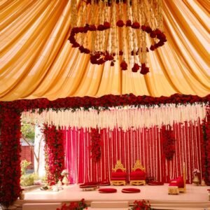 Elegant wedding ceremony setup with red roses, gold accents, and draped fabric in a luxurious setting.